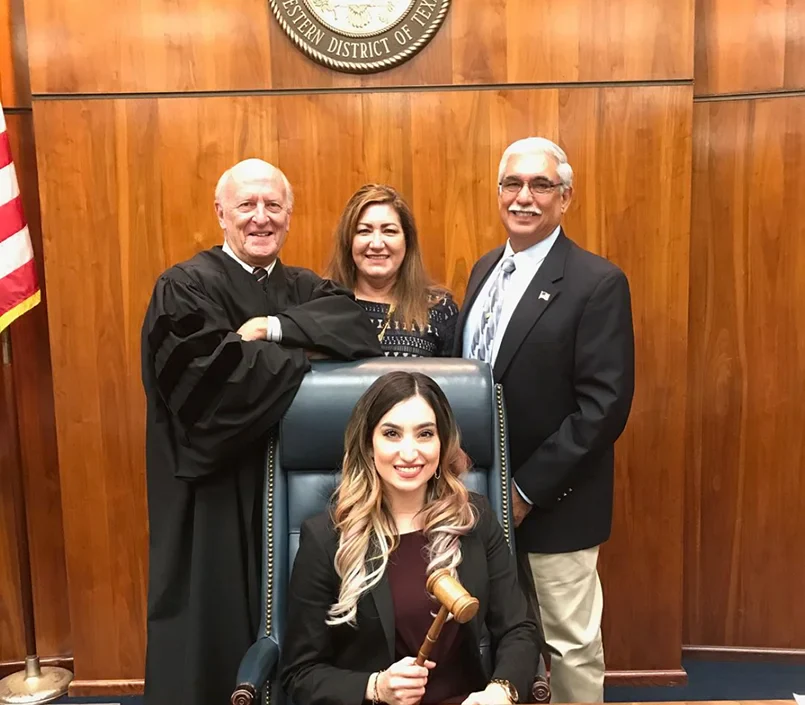 Attorney Amanda Hernandez holding a gavel sits in a chair, with a judge and two other adults